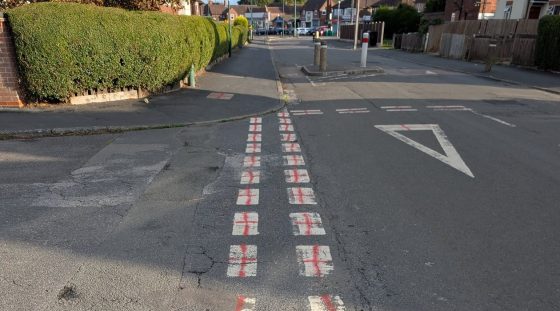 A road with red St George's crosses crudely spray painted onto white road markings