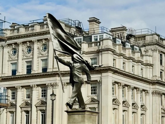 Banksy statue in central London showing a man walking with his face obscured by a huge flag wrapped around it (that he is holding)